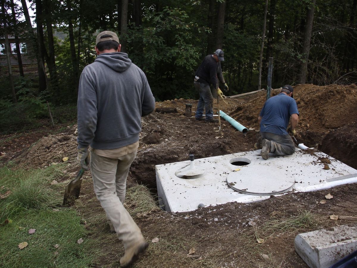 Crew setting a new concrete septic tank into an excavated pit